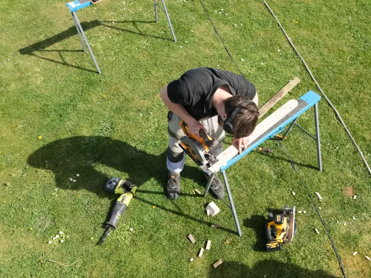 Tradesman cutting timber on a saw horse in a garden